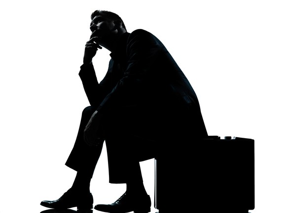 Silhouette of a man sitting on his briefcase, apparently in deep thought.