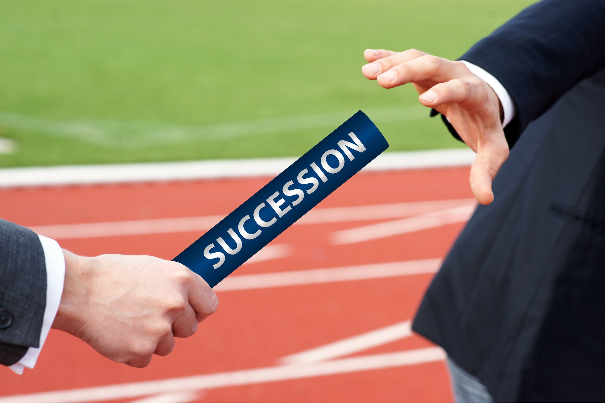 A man in a suit on a track handing a baton marked "succession" to another man in a suit. 