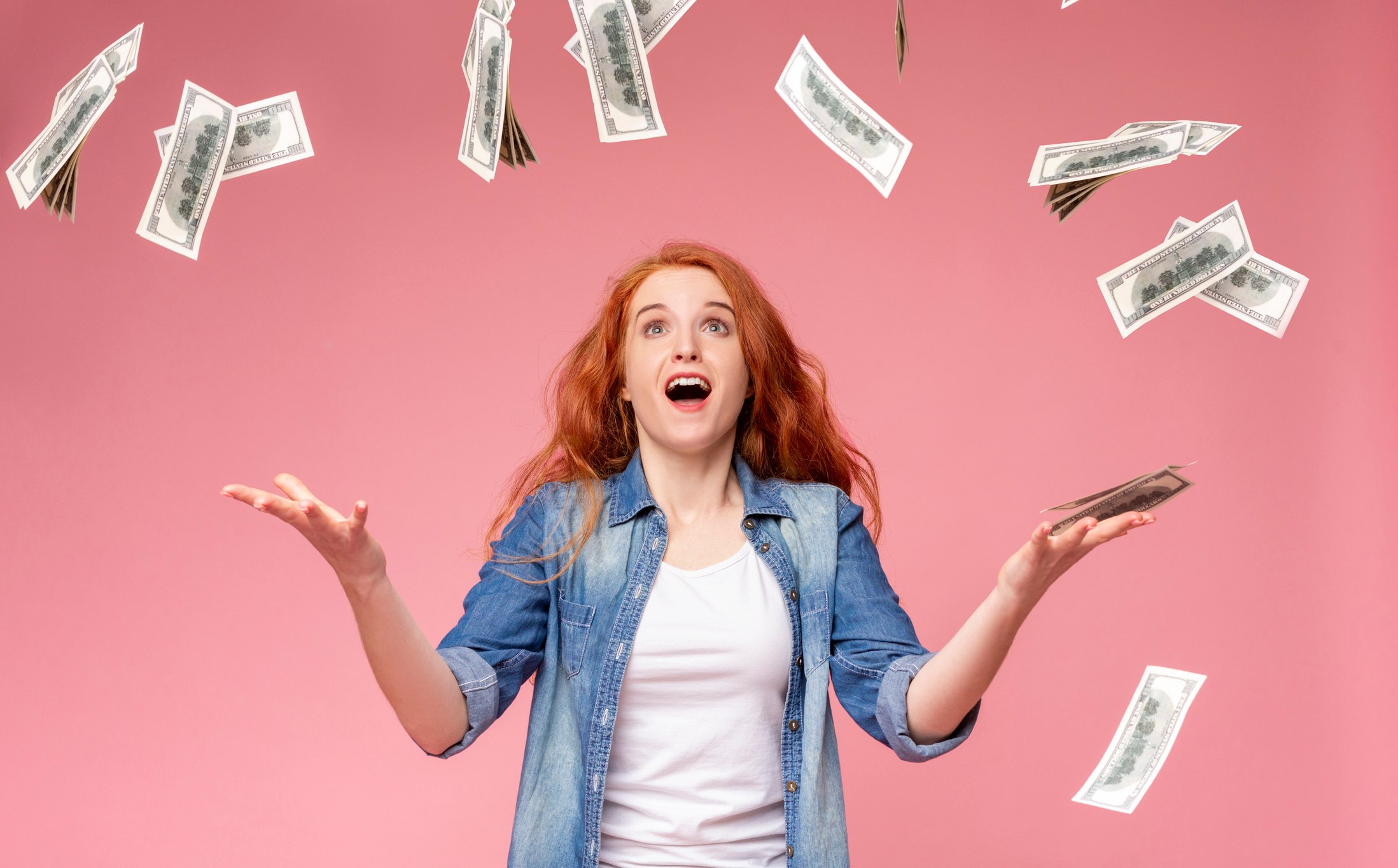A young woman is surprised as hundred-dollar bills rain down from the sky.