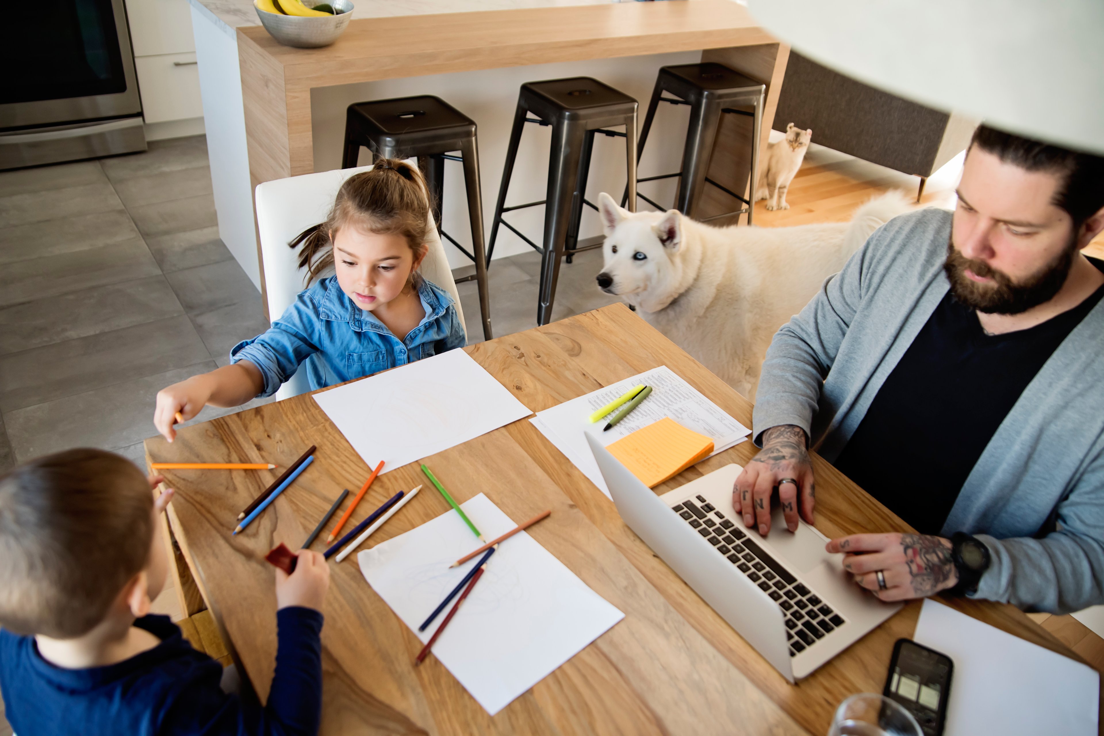 Dad working at home with his two kids at a kitchen table. 