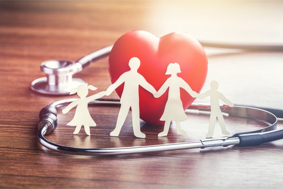 A paper cutout of a family holding hands with a heart in the background and a stethscope.