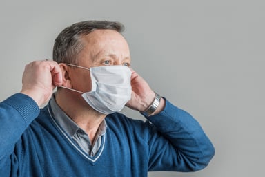 Older man putting on mask_GettyImages-1218543636