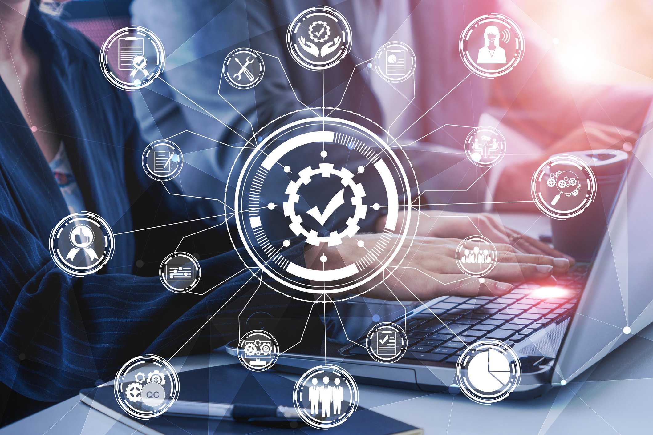 Business person using laptop overlaid with network graphic with different functions in circles representing functions like users, graphs, setup, and search.