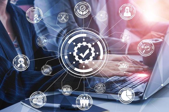 Business person using laptop overlaid with network graphic with different functions in circles representing functions like users, graphs, setup, and search.