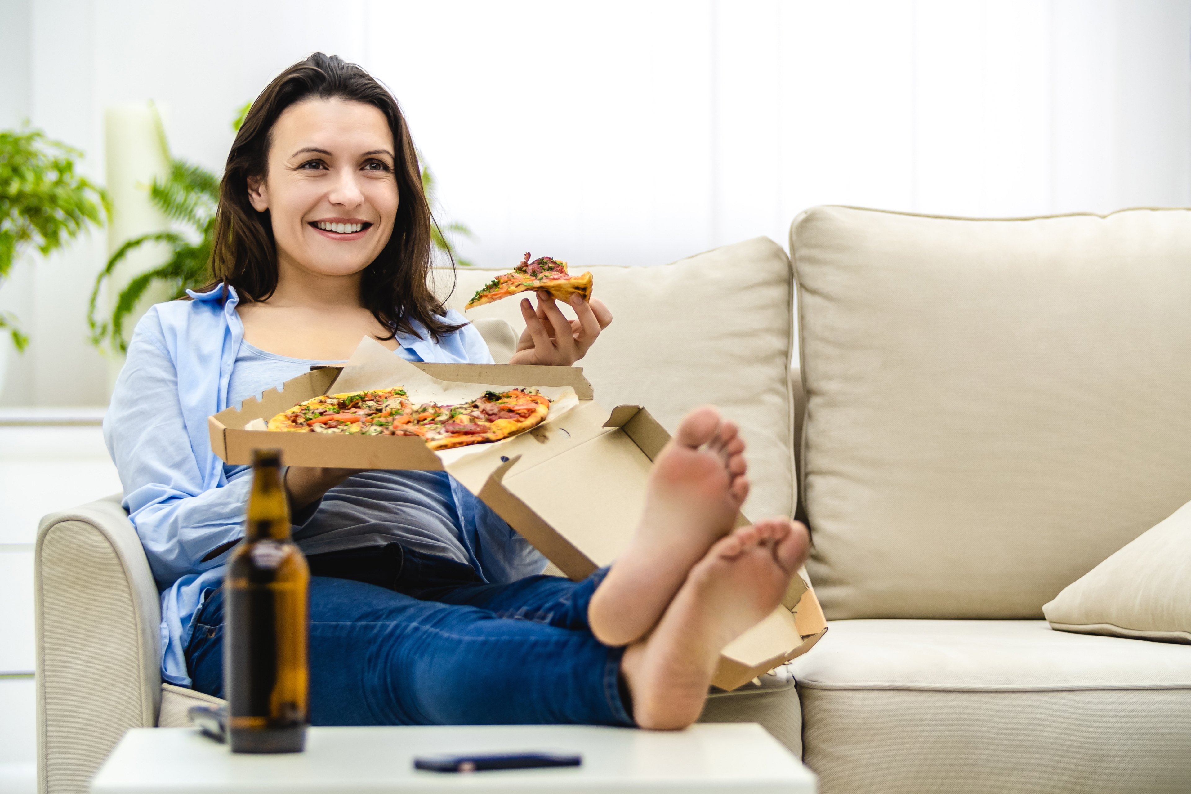 A woman eating pizza on her couch at home