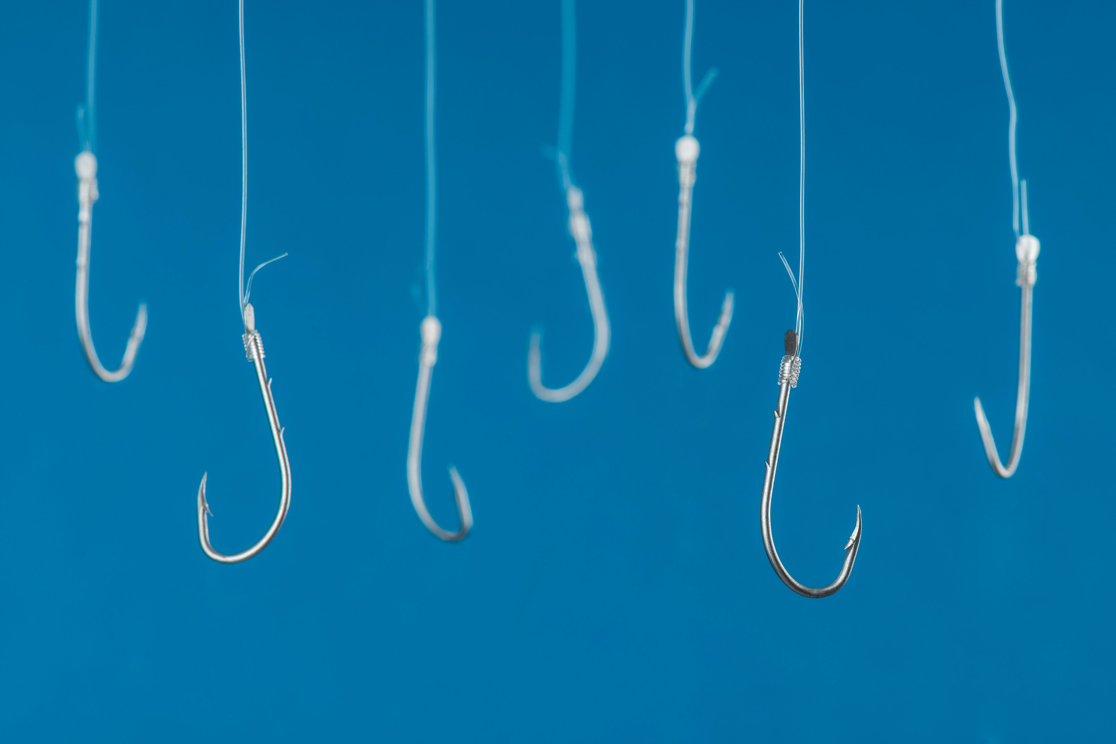 A series of fishing hooks tied to lines against a blue background. 