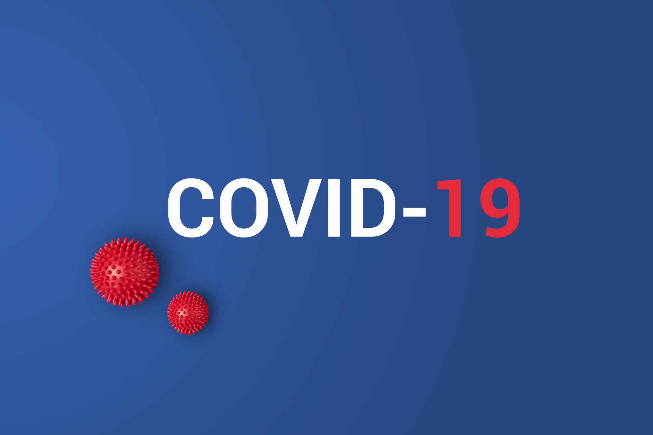COVID-19 printed against blue background with red plastic balls representing the coronavirus