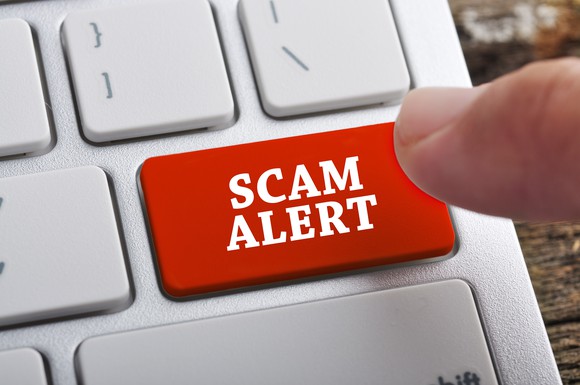 Finger hovering over a red computer keyboard button reading Scam Alert.