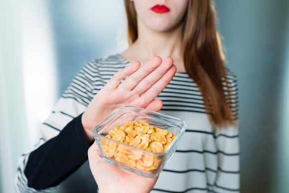 Woman giving "no" hand gesture to a box of peanuts. 