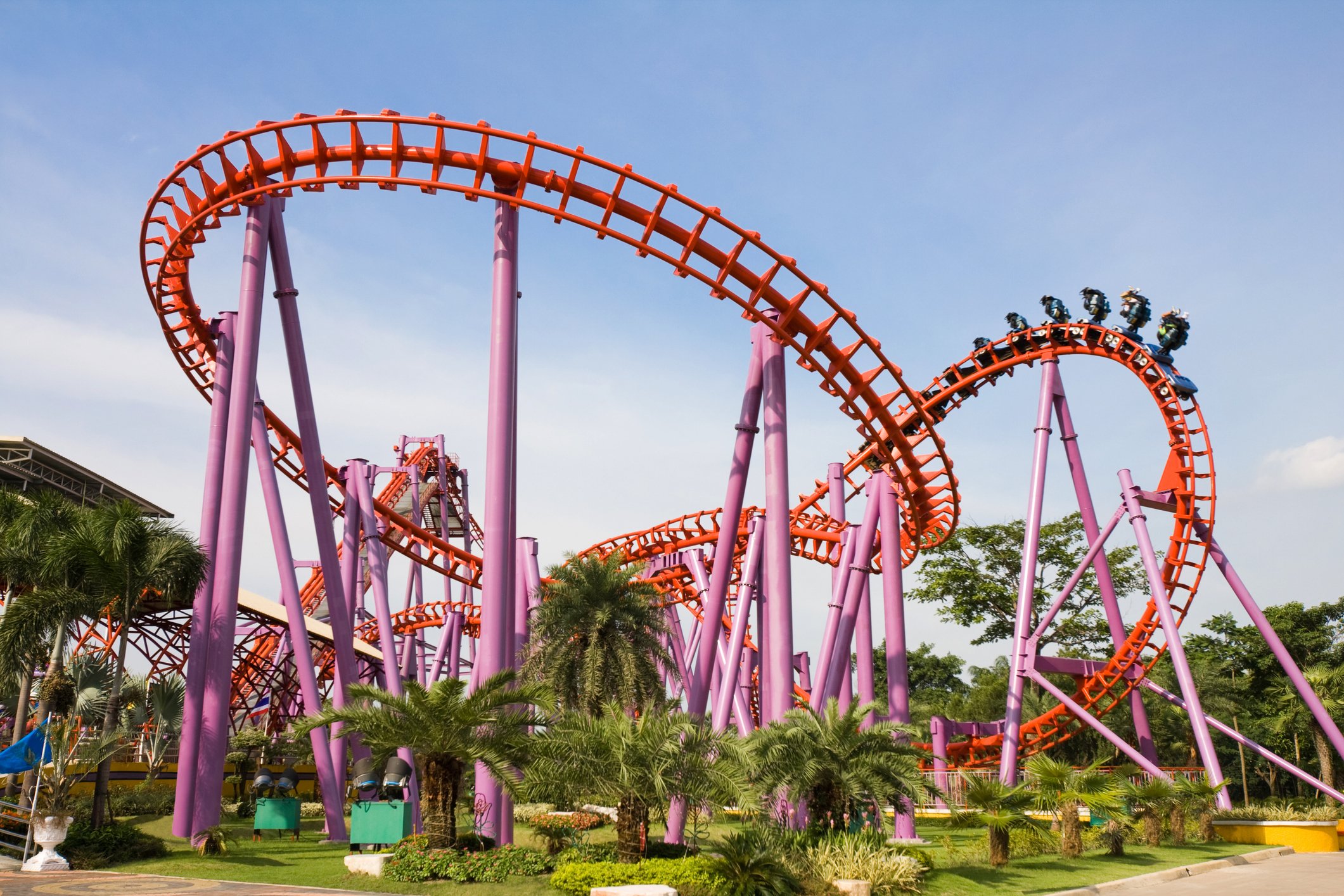 A pink and red roller coaster surrounded by tropical vegetation