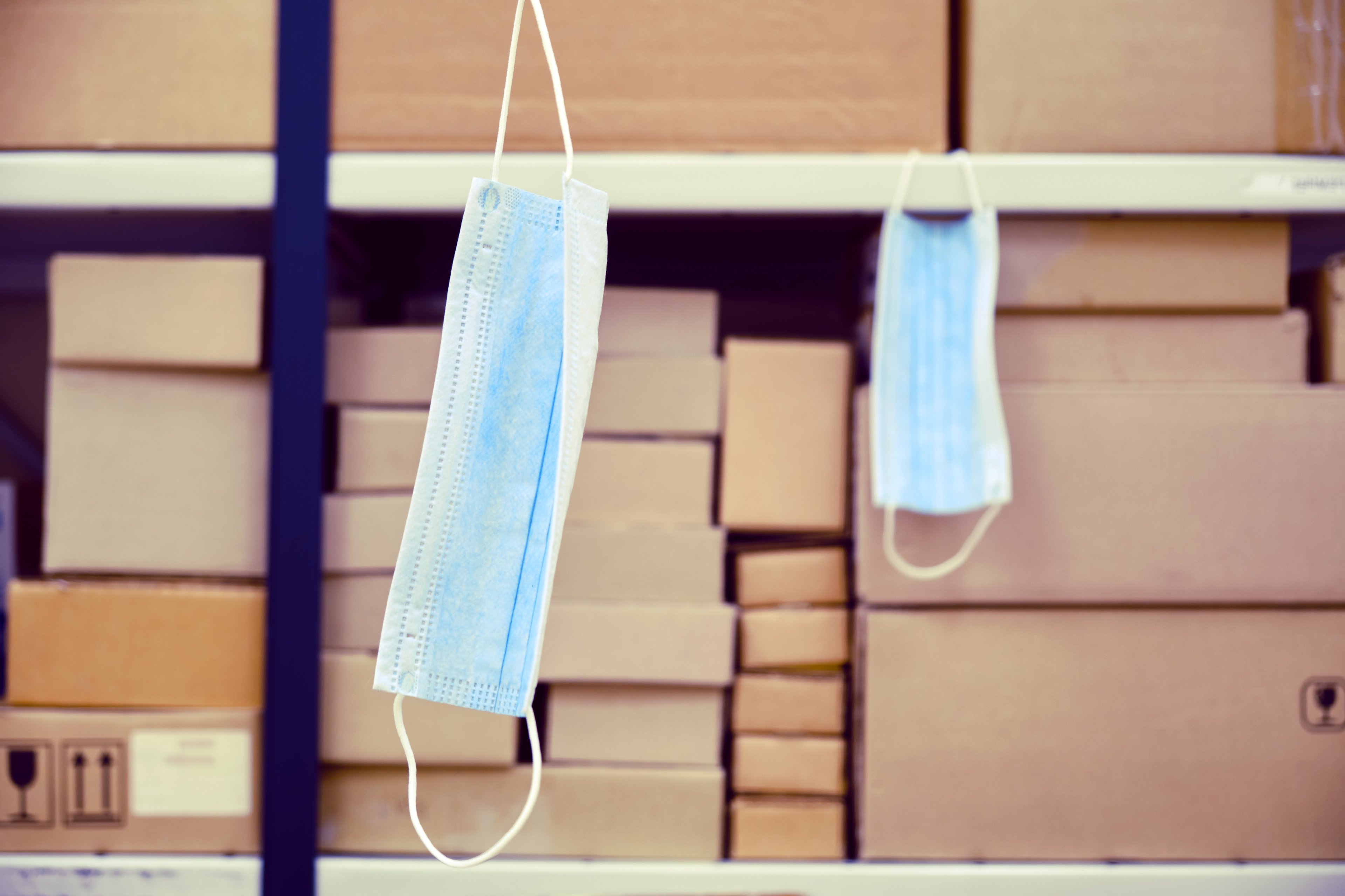 A warehouse with boxes and two surgical masks hanging off of some of them. 