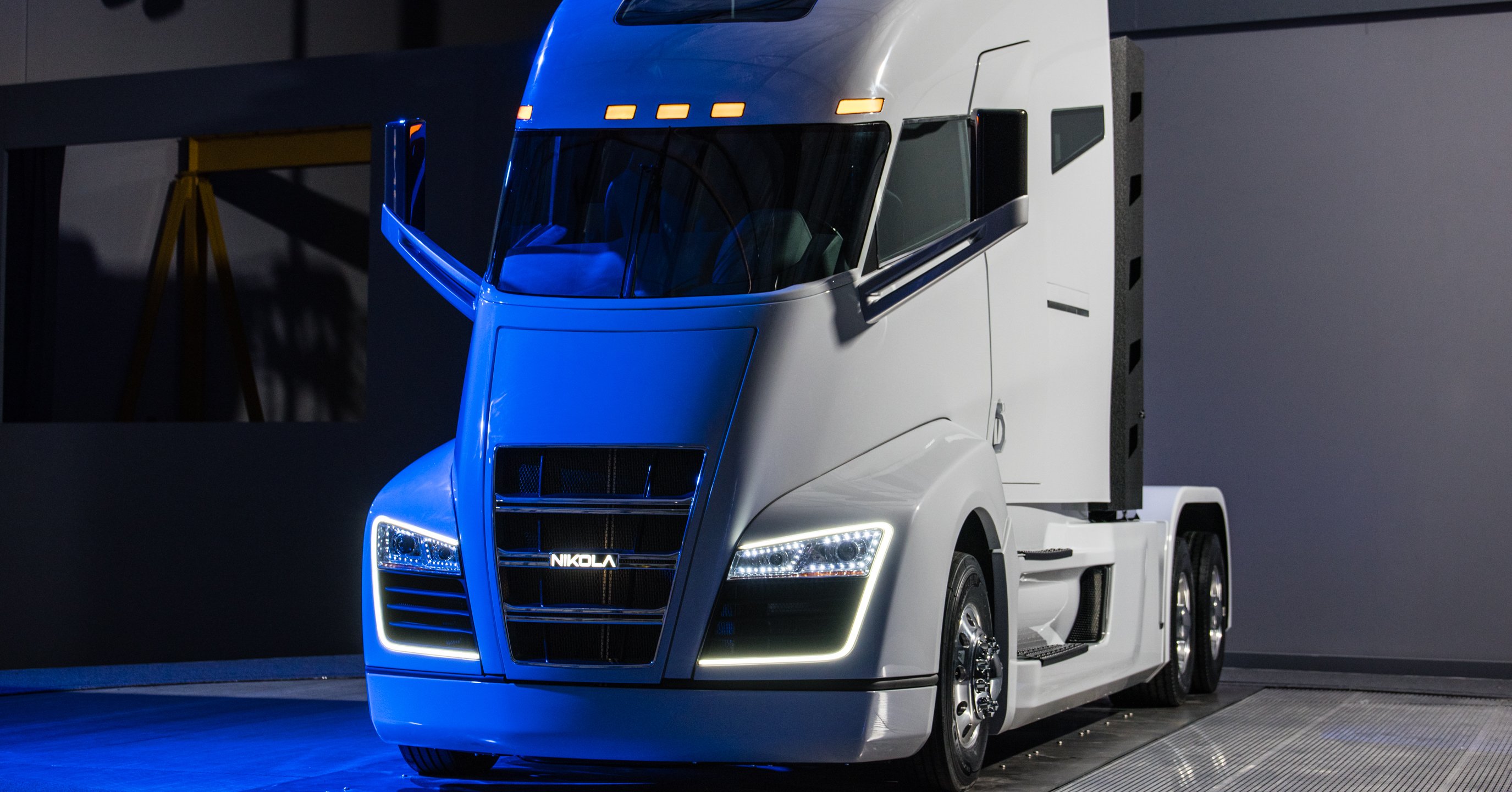 A while Nikola One semi truck, parked in a garage and illuminated by blue light.