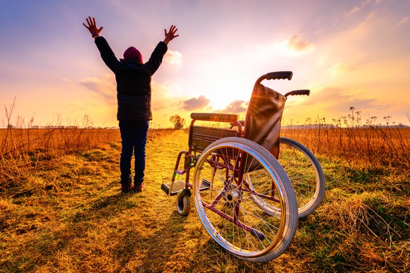 Woman raising her hands high after getting off wheelchair. 