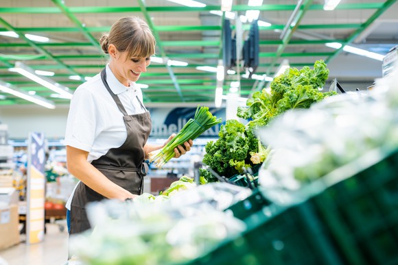 A grocery employee restocking vegetables.