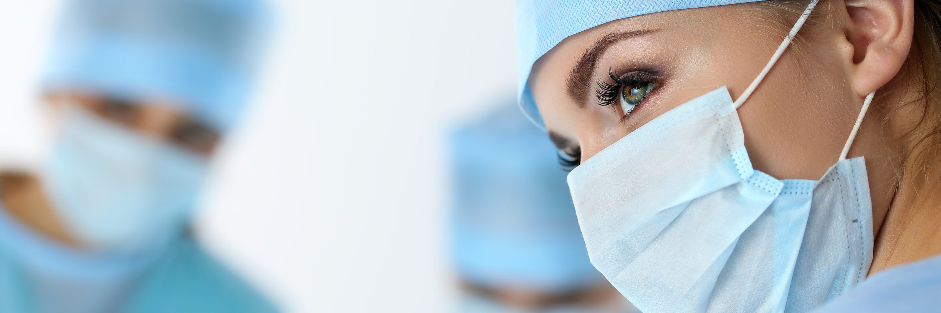 Close-up photo of a female doctor wearing a safety mask with two other doctors in the blurred background.