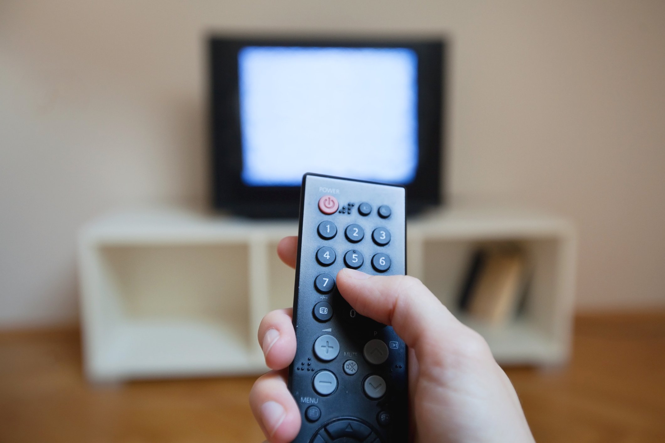 Closeup on a hand holding a television remote with a static-filled TV in the background.