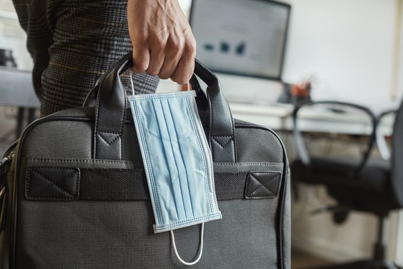 Man holding a briefcase and a face mask.