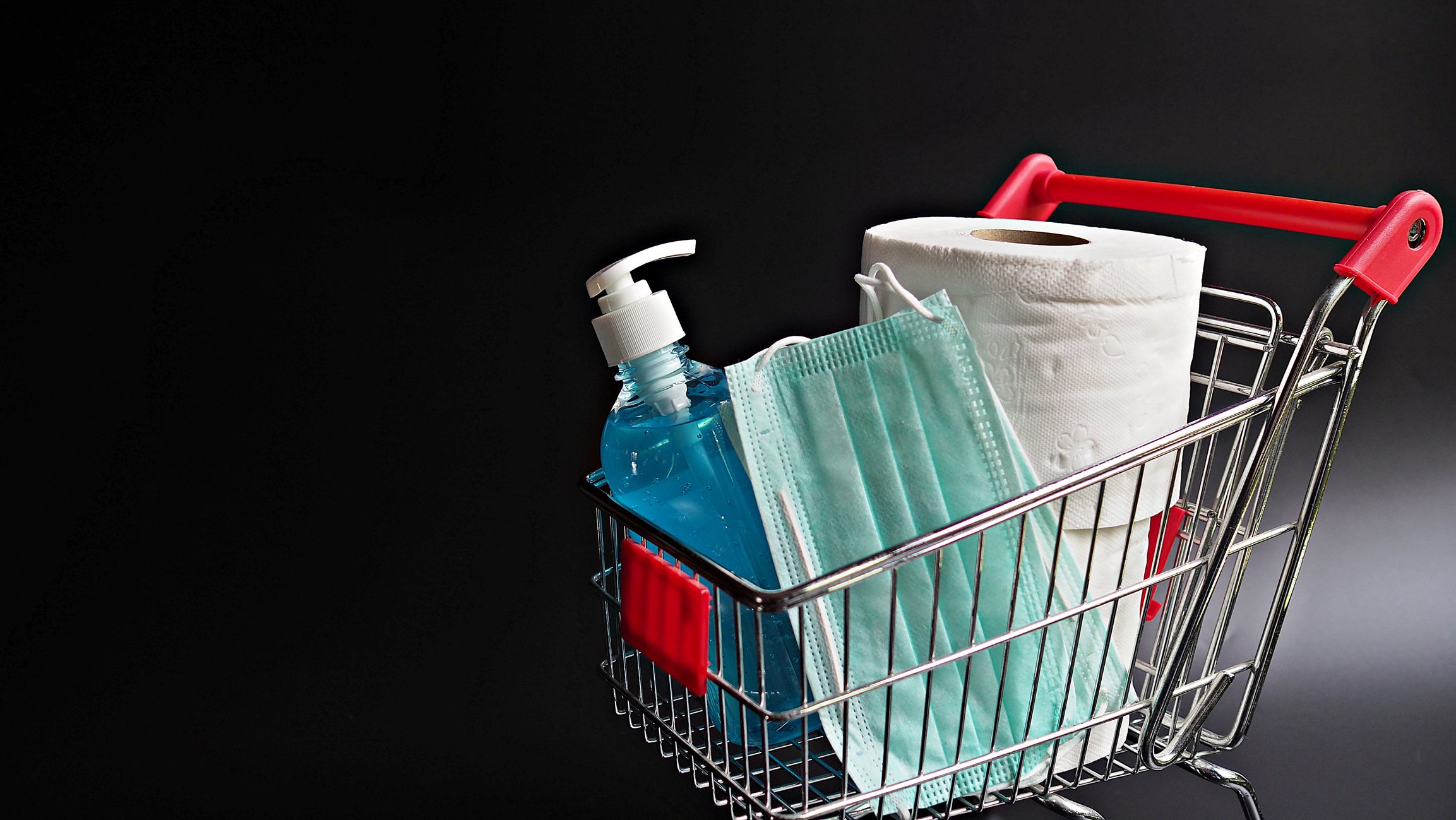 A shopping cart filled with toilet paper, sanitizer, and a mask