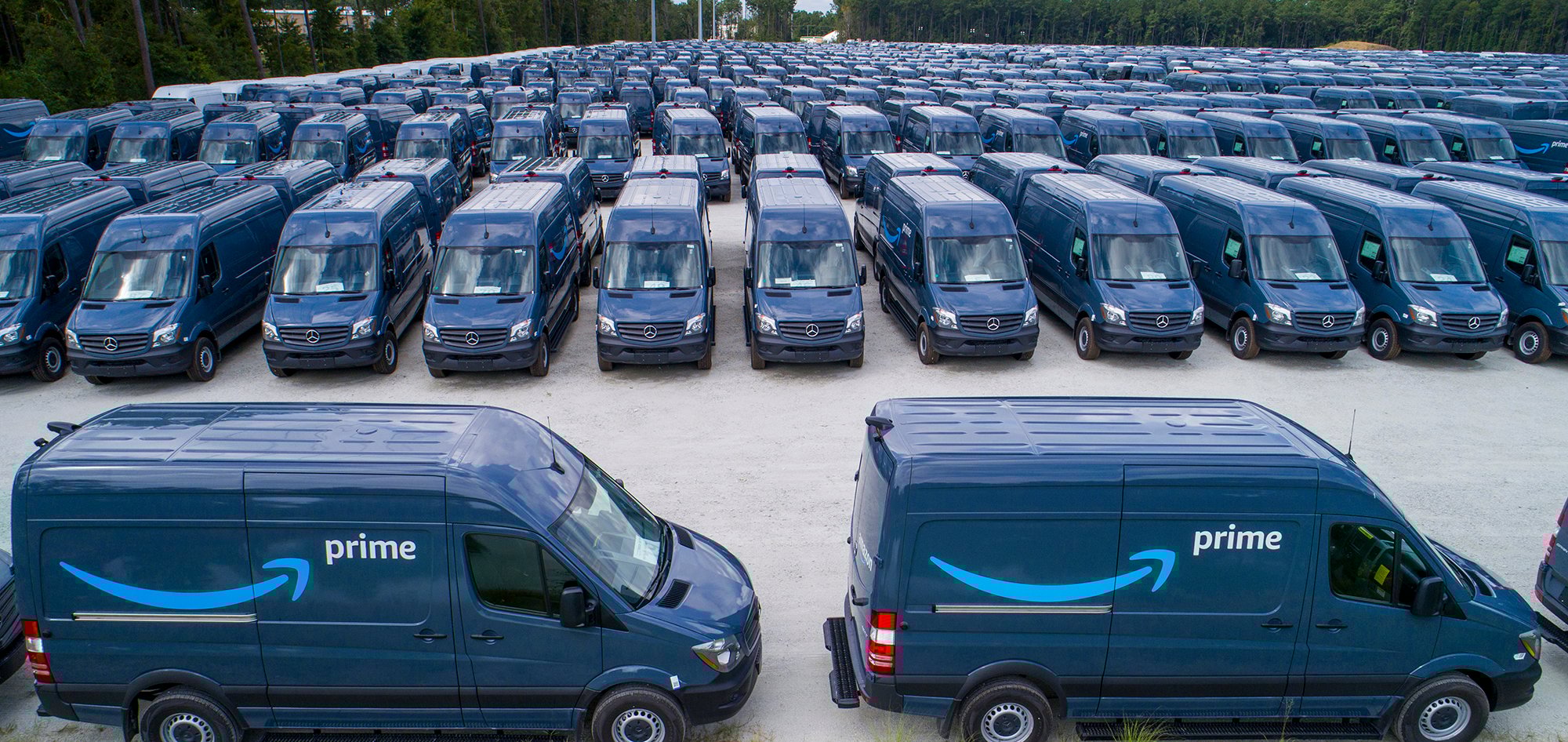 Several rows of blue vans with the Amazon Prime logo in a parking lot.