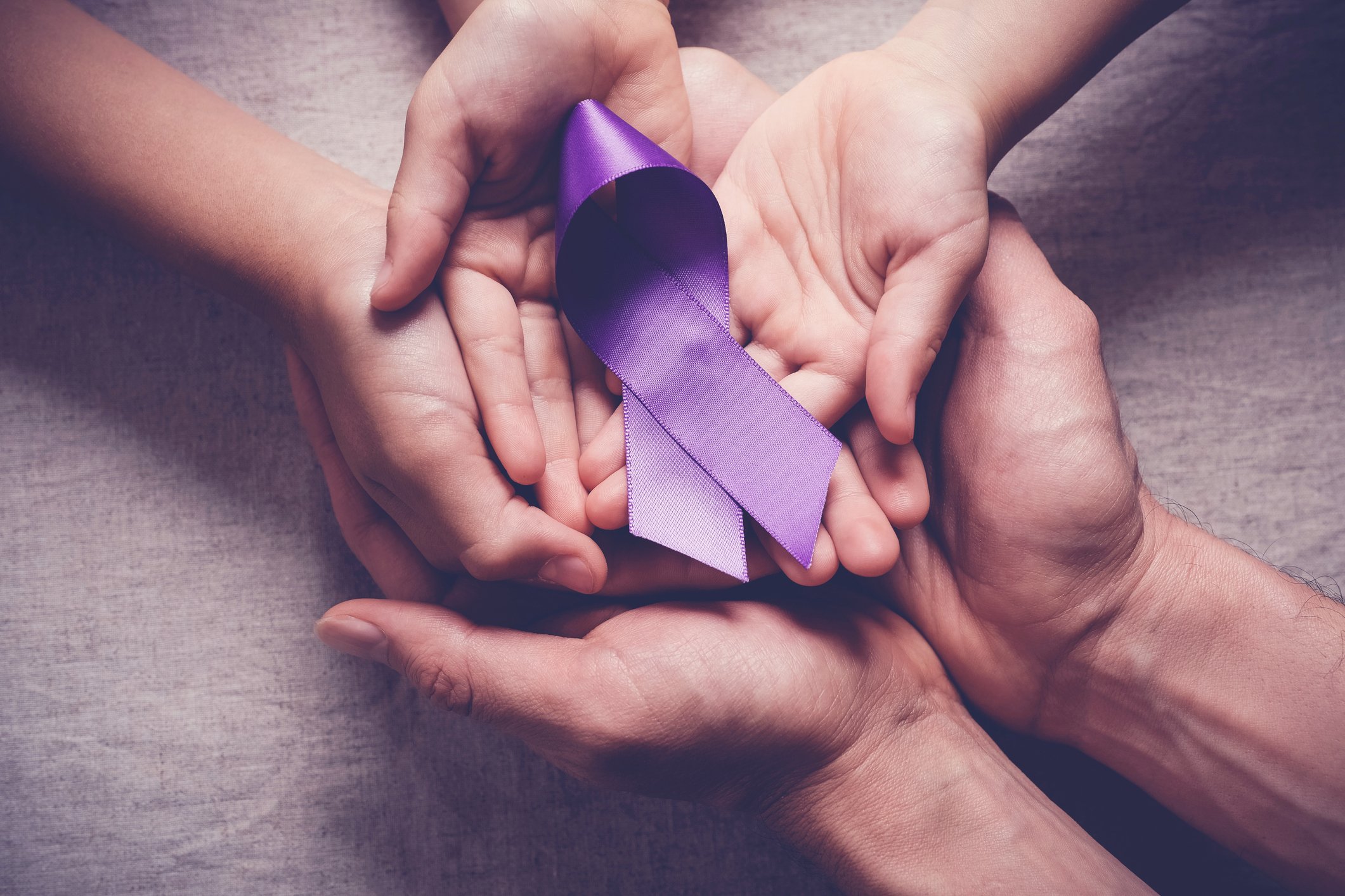Three sets of hands holding a purple cancer ribbon. 