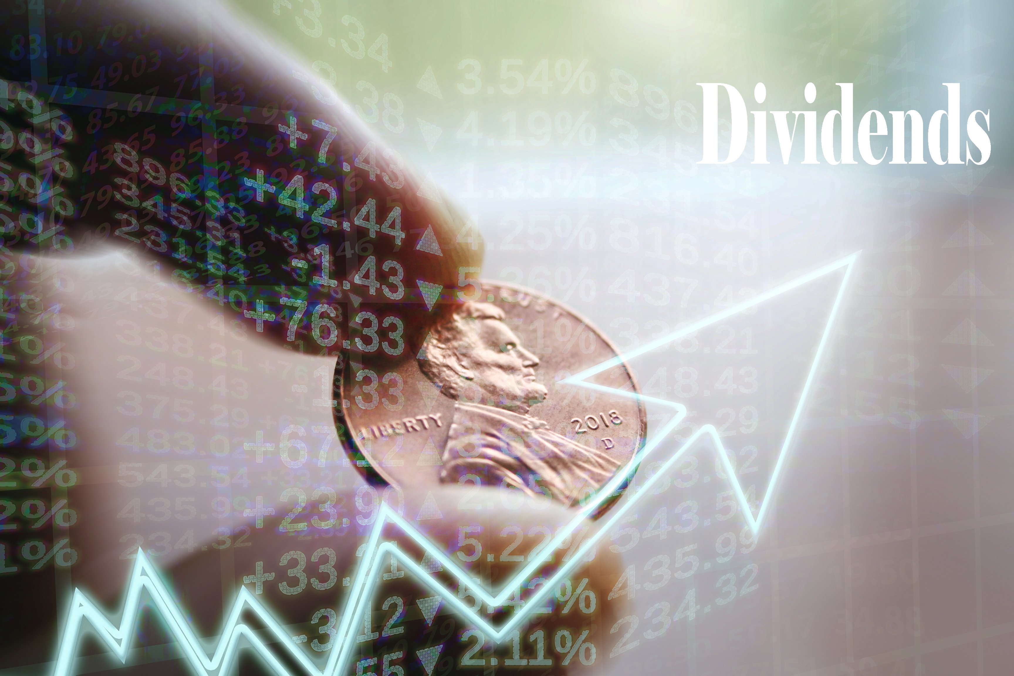 A person's fingers holding a penny behind a rising chart pointing to the word "dividends."