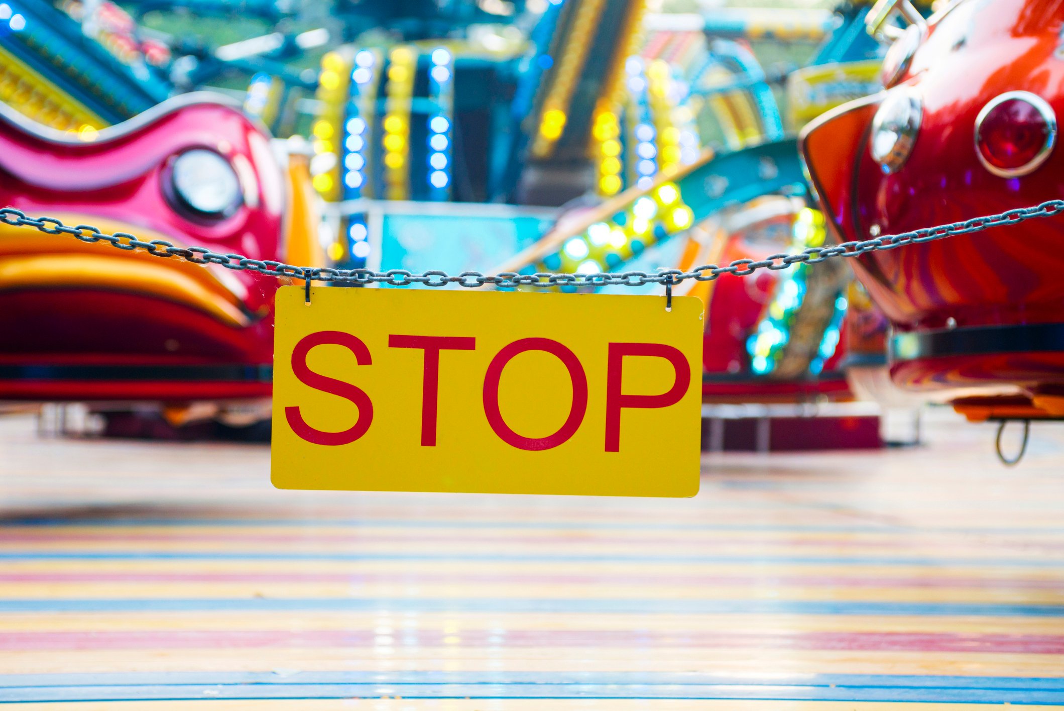 A chain with a sign saying stop that is in front of a ride.