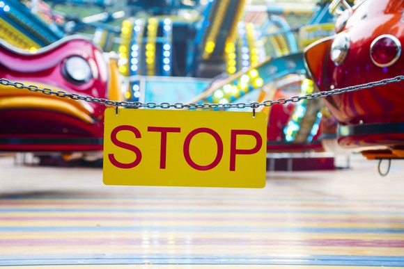 A chain with a sign saying stop that is in front of a ride.