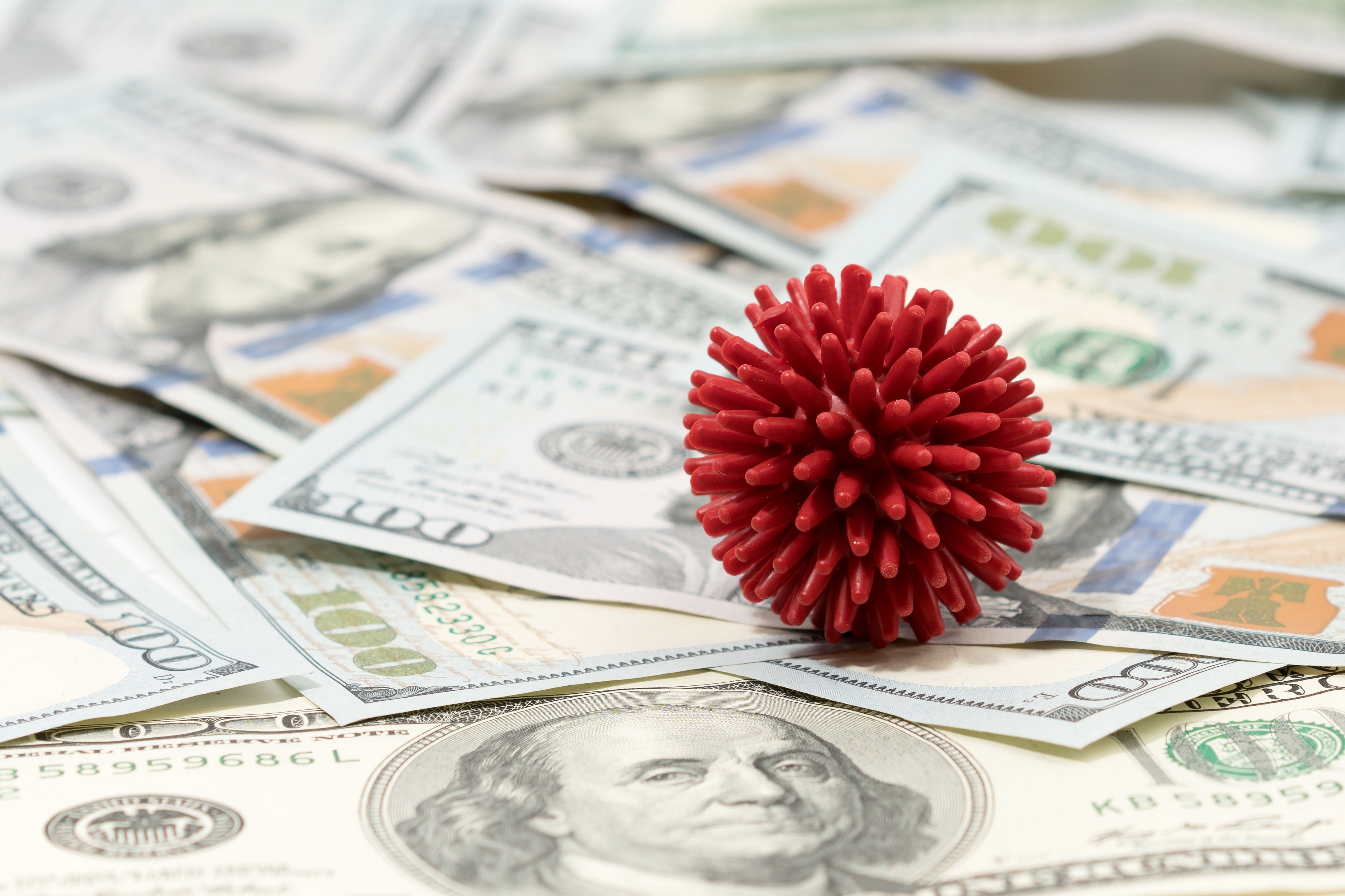 A red coronavirus model on top of a messy pile of $100 bills