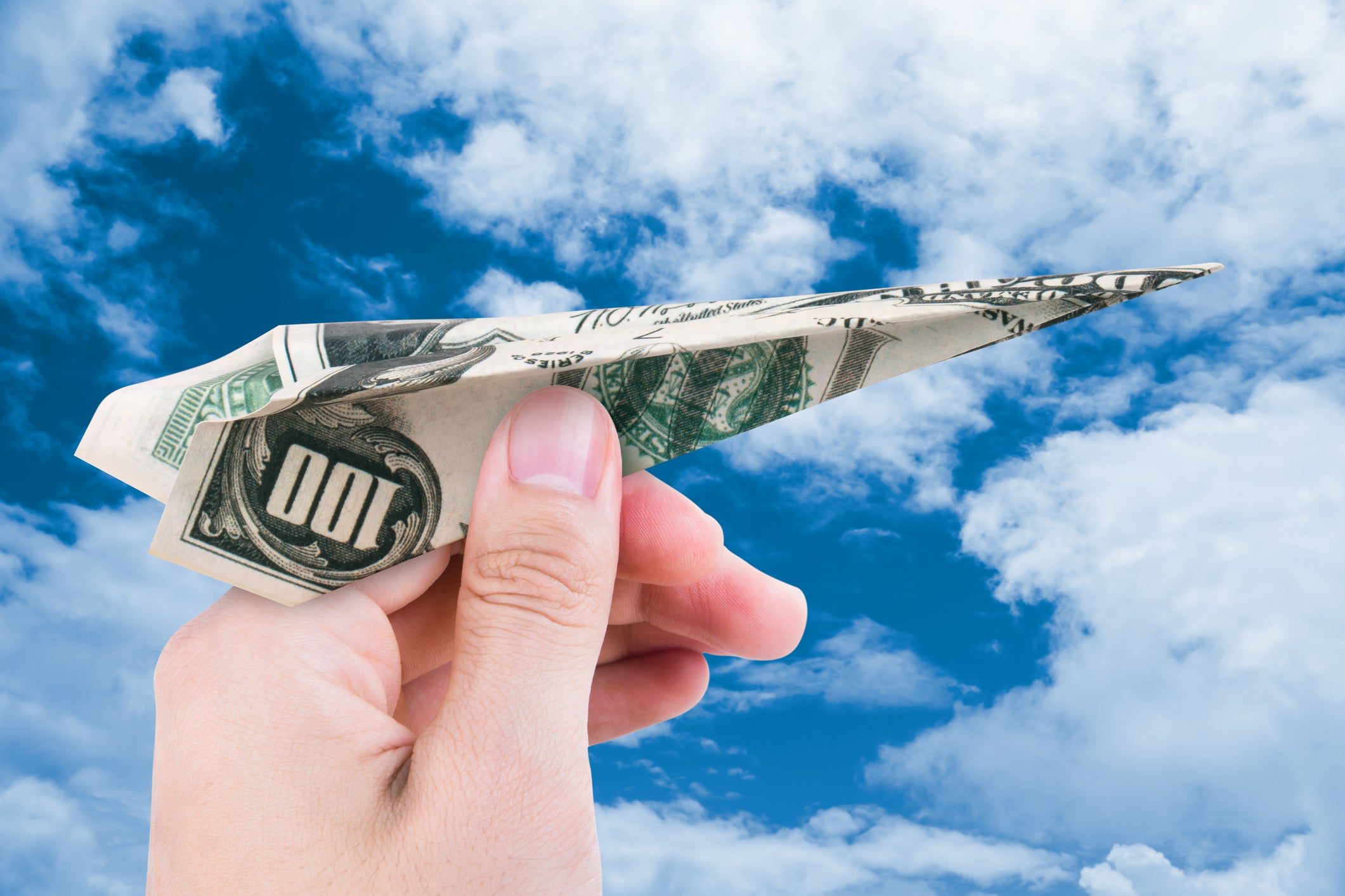 A 100-dollar bill as a paper airplane against a backdrop of clouds.