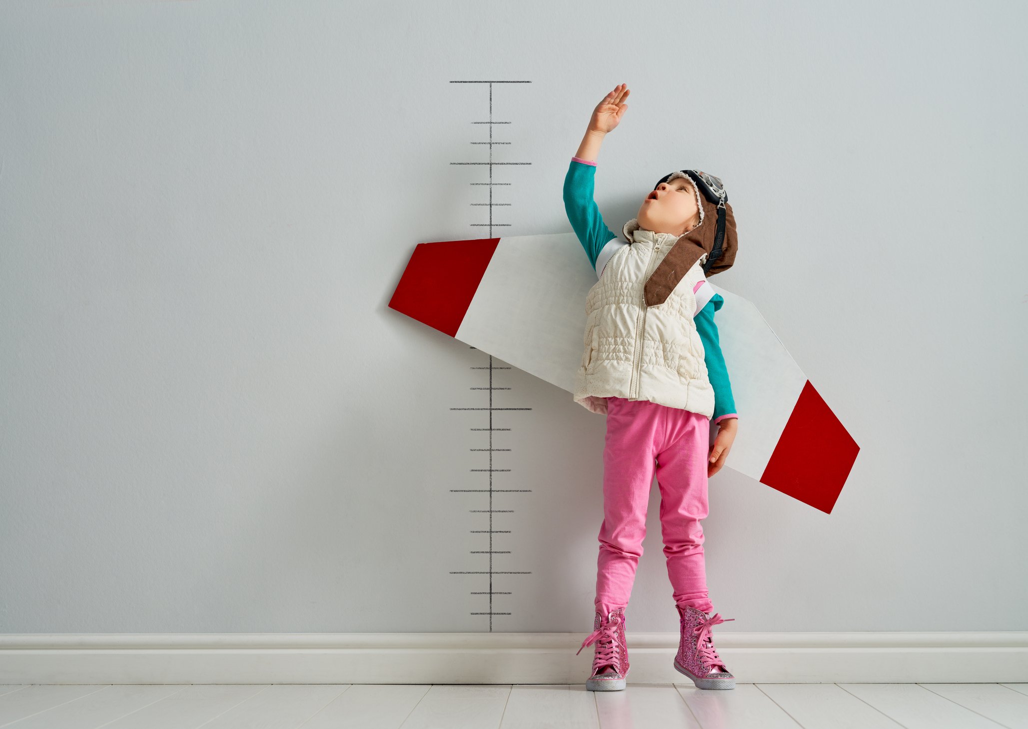 A kid wearing paper wings measuring herself against a ruler drawn on a wall.