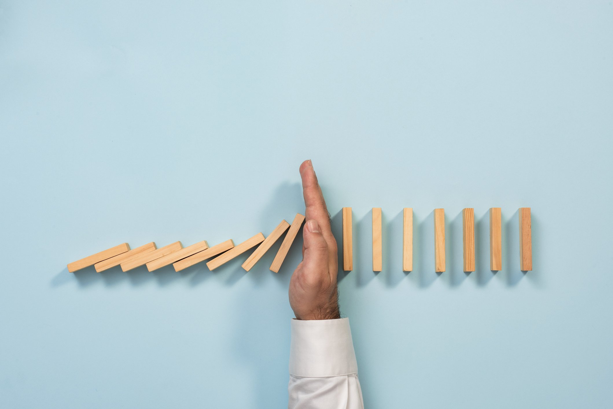 Man stopping dominoes from falling by placing his hand between them.