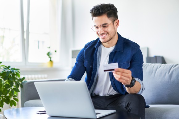 Man holding credit card and smiling while looking at laptop