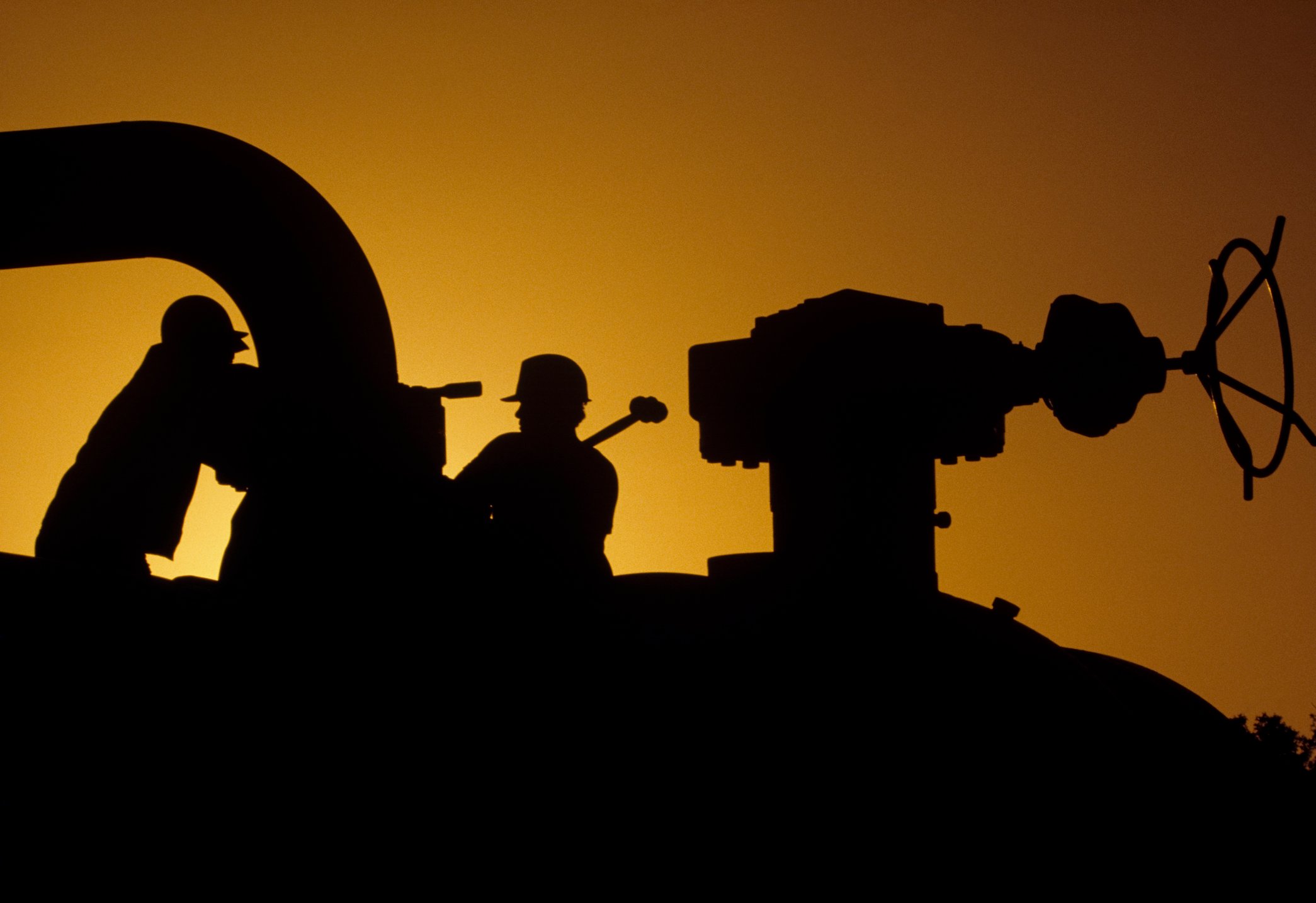 Silhouette of workers operating on a pipeline at sunset. 