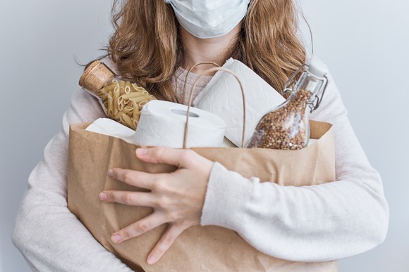 A woman wearing a mask holding a grocery bag full of essentials.
