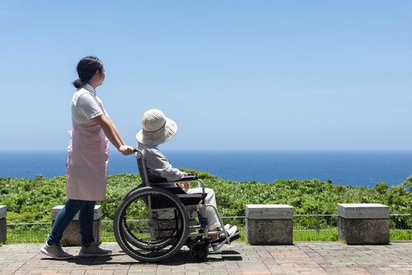 A caregiver pushes an elderly woman in a wheelchair.