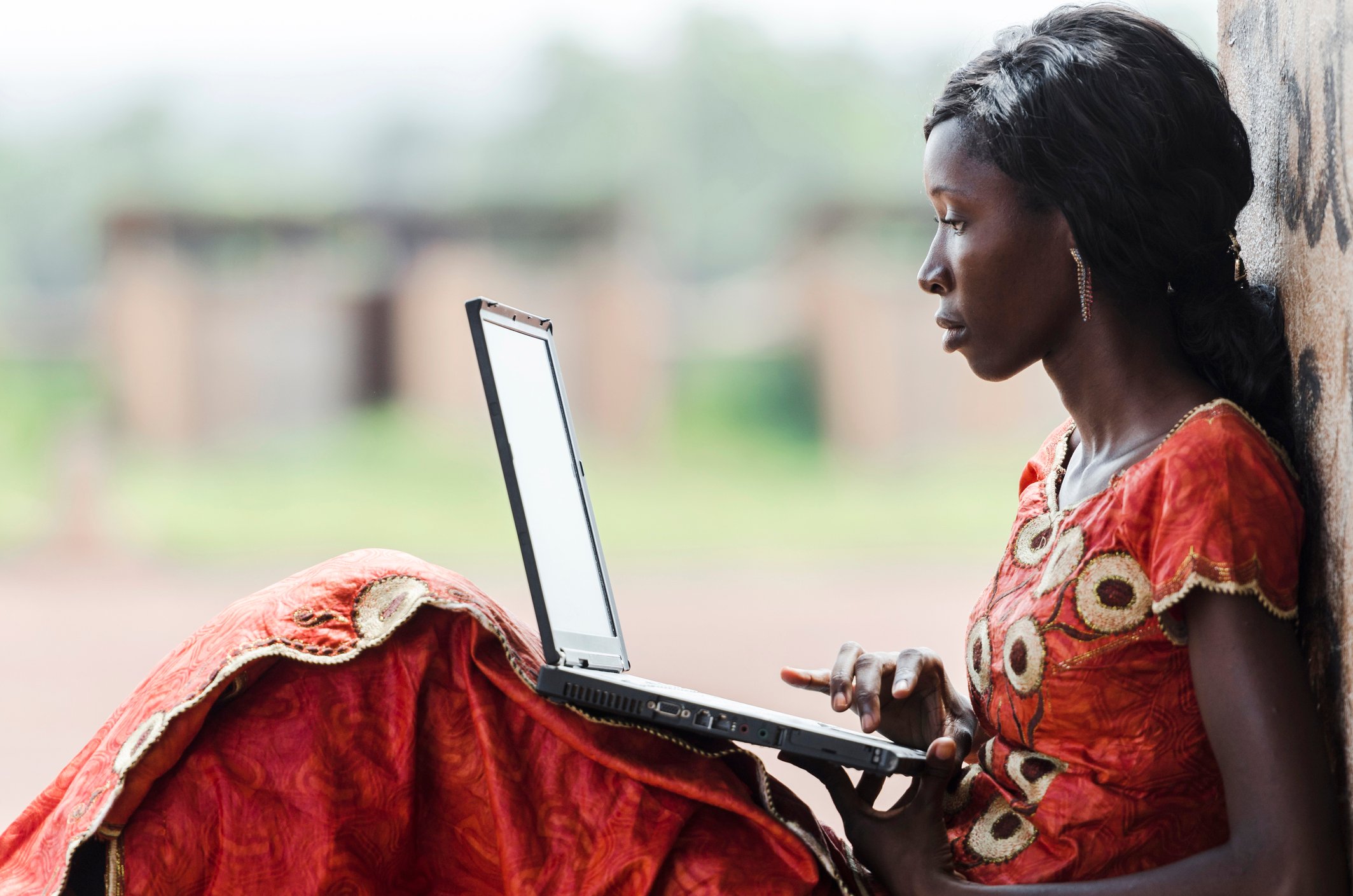 A young African woman uses a laptop outside.