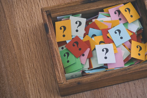 A wooden box holding many note cards each displaying a question mark.