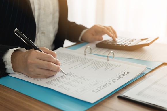 A man checking figures on a balance sheet while using a calculator