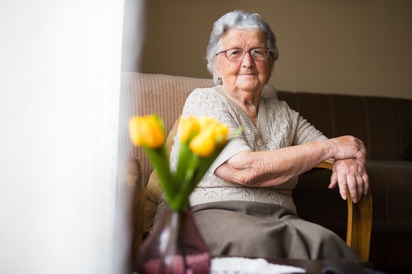 Woman in nursing home sitting by a table with a vase of tulips. 