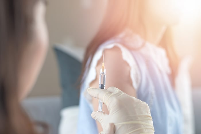 Gloved hand holding up syringe in front of patient's exposed arm