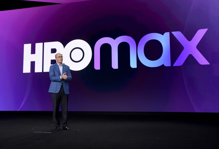 John Stankey on stage in front of a screen displaying the HBO Max logo.