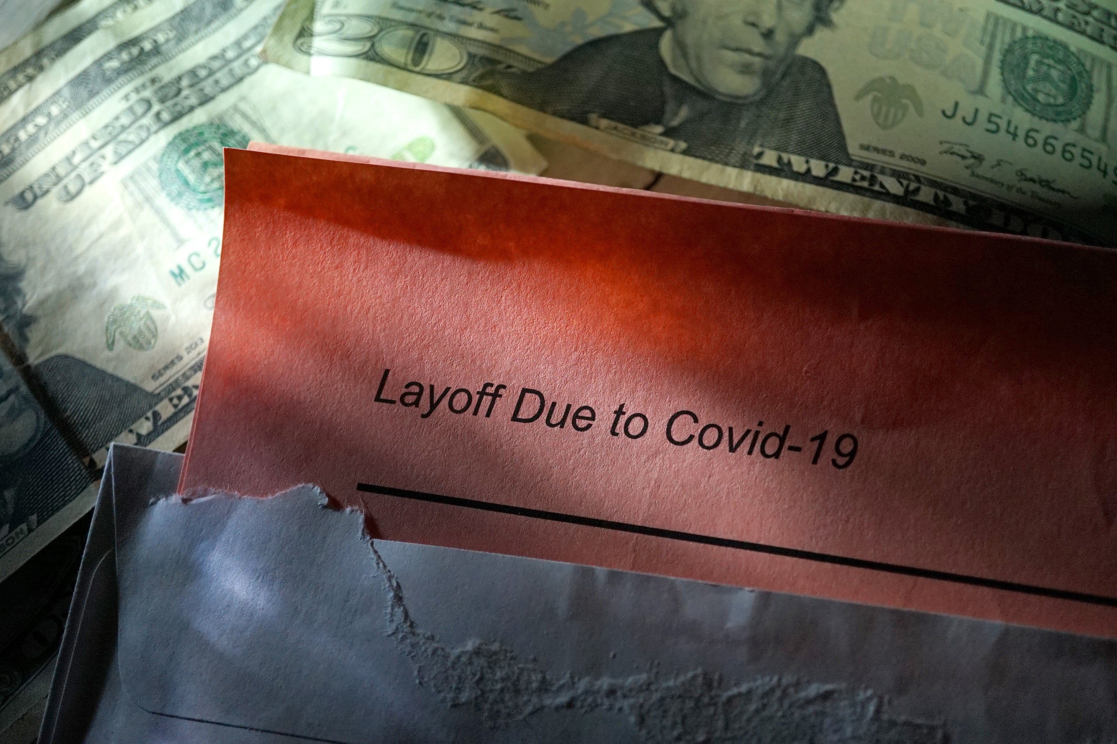 A layoff sign due to COVID-19 with money in the background. 
