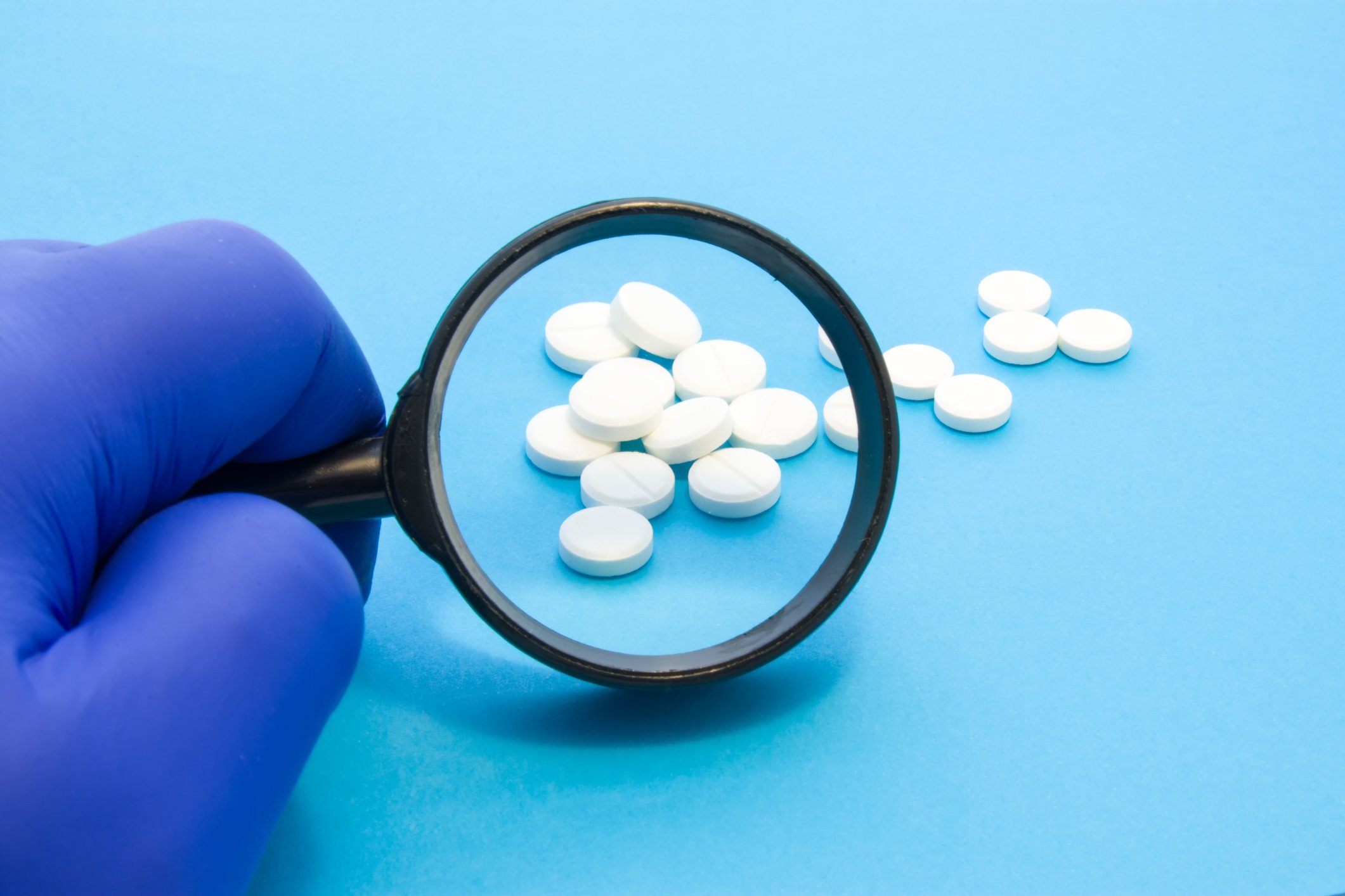 Holding up a magnifying glass in front of several white pharmaceutical pills.