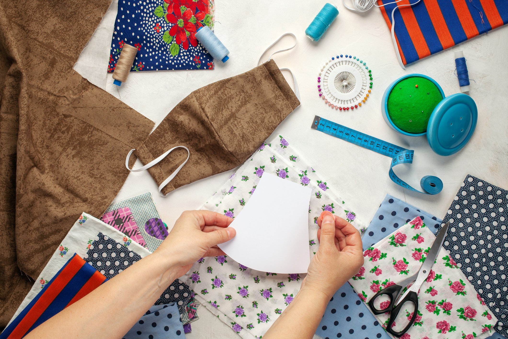 A craft table viewed from above as someone makes face masks out of various fabrics