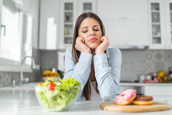 Woman trying to decide between salad and donut.