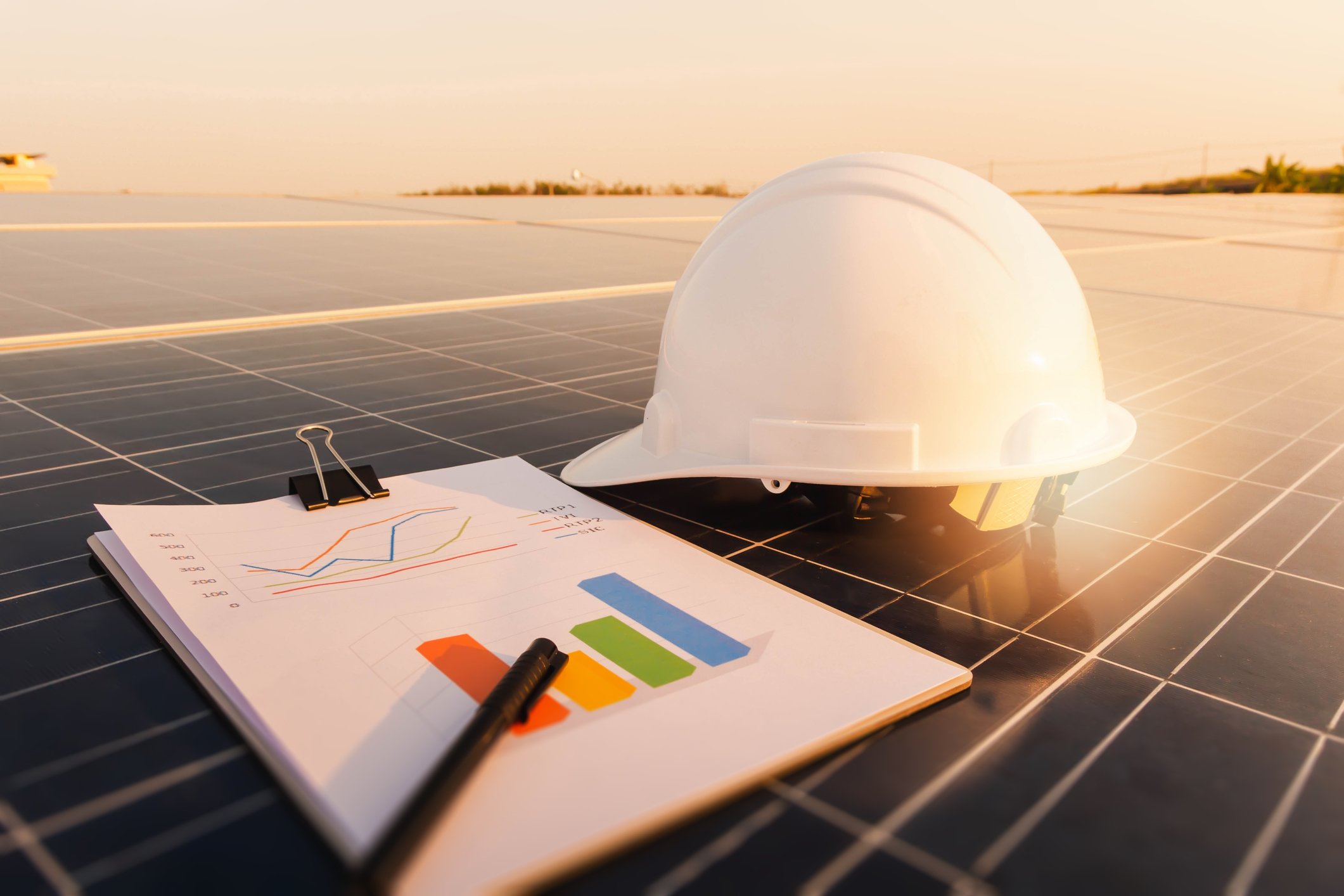 An engineer's hard hat and clipboard rest on solar panels.