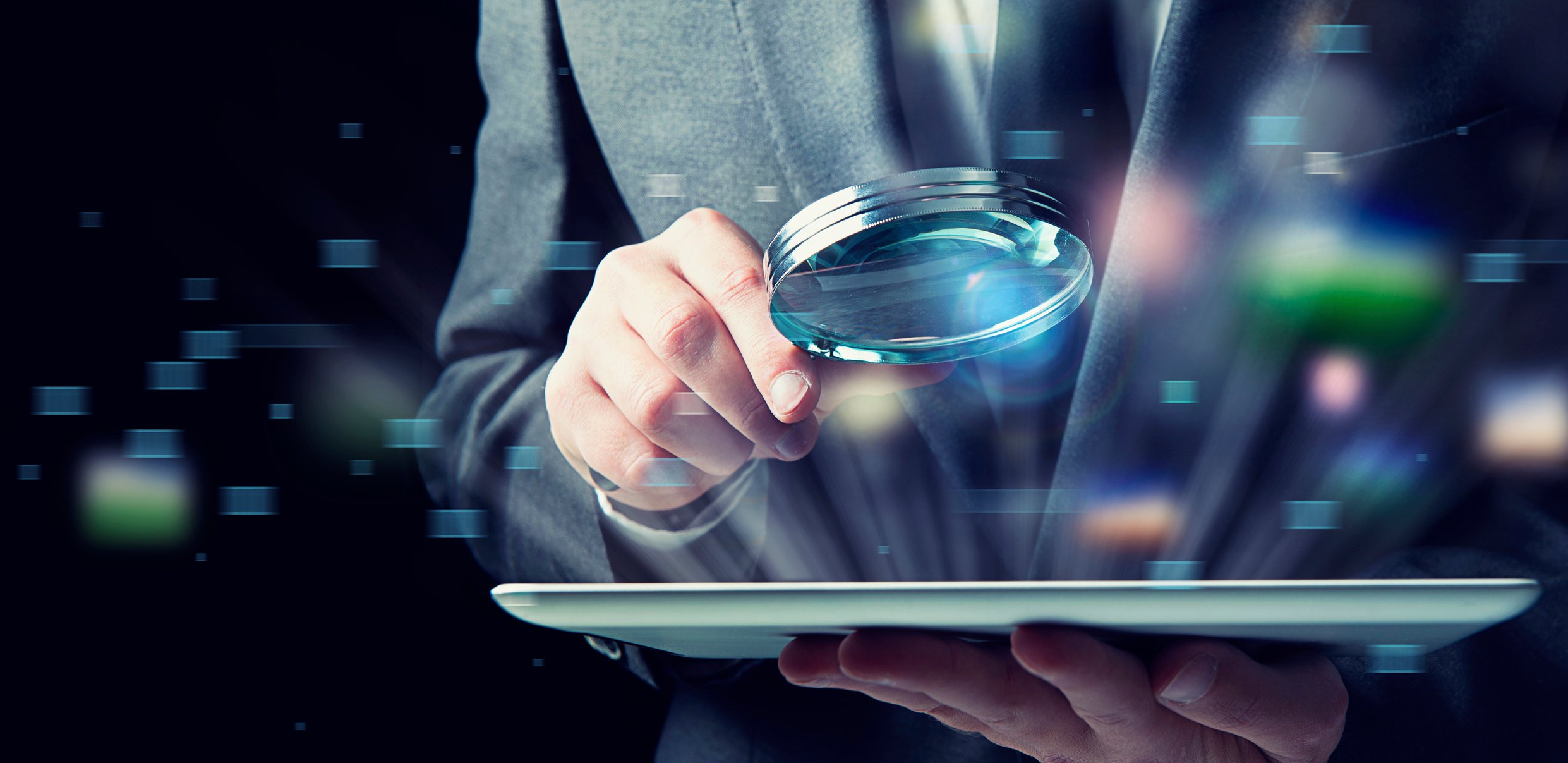 Closeup of a businessman holding a magnifying glass to an electronic tablet. 