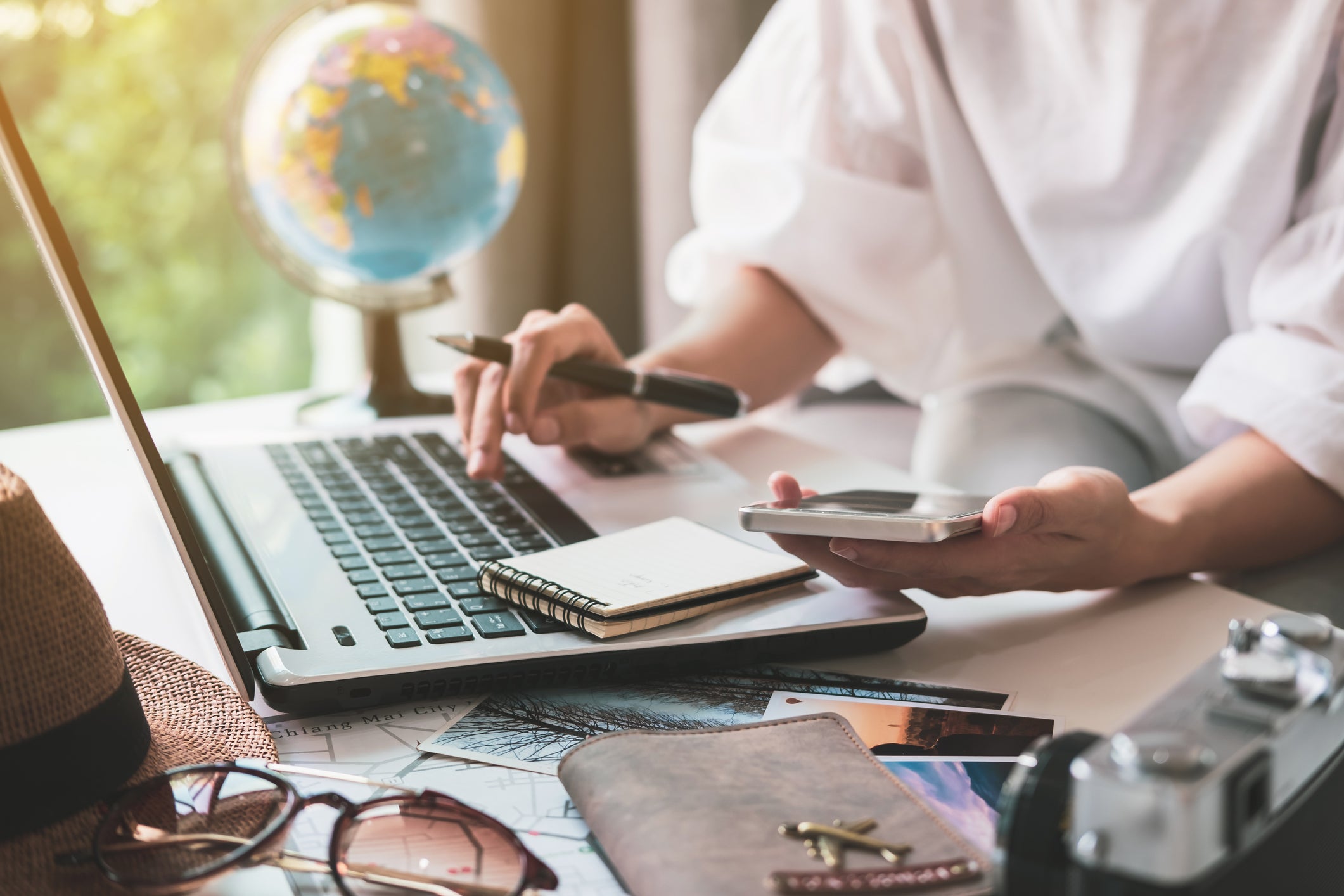 A woman working on a phone and laptop with a globe in the background.