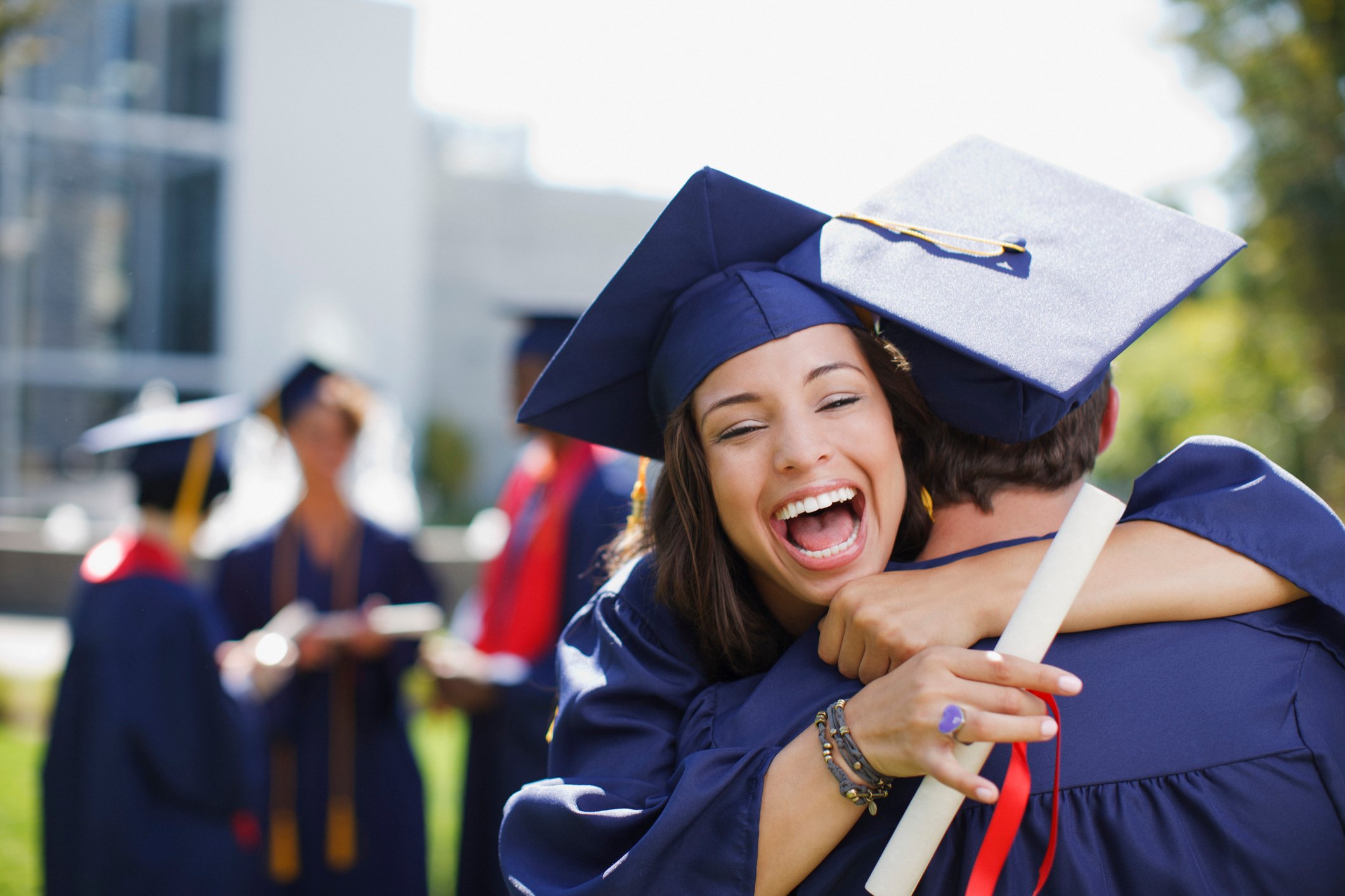People in graduation caps and gowns hugging each other