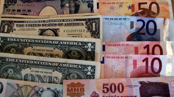 US dollar bills splayed out on a table along with currency from around the world. 